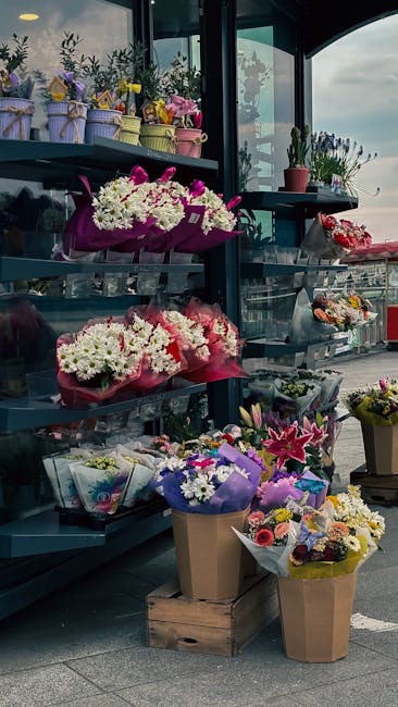 An outdoor display of fresh floral arrangements and bouquets at a flower stand, featuring a variety of colorful flowers including white daisies with purple accents, pink lilies, and mixed seasonal blo